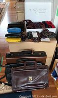 Overview showing several leather briefcases, belts, and suspenders arranged with white boxes containing suspenders and belts, some belts coiled with rubber bands.