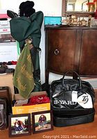 Green Hogan golf bag with clubs and black leather S-Yard bag with Harrods towel and two ceramic golf pictures in wood frames