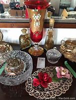 Full view of crystal, porcelain roses, Venetian red vase, potpourri bowl, and sealed bottles on a reflective surface