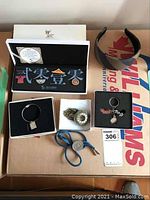 Full lot overview showing all items including pins in box, bracelet, pocket watch, Calgary dollar on cord, shell key change, and headband