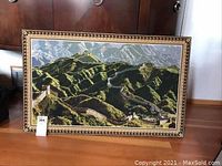 Full view of the framed needlepoint picture showing the Great Wall of China in a landscape scene on wood floor.