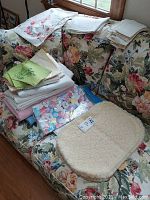 Lot of vintage table linens including runners, napkins, placemats, and tablecloths displayed on floral sofa.