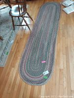 Full view of the braided runner rug placed on wooden floor, showing oval shape and size relative to furniture.