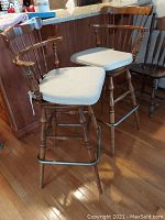 Two wooden Ethan Allen swivel bar stools with beige cushions, positioned near a kitchen counter.