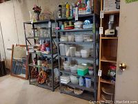 Wide shot showing three black metal shelving units stocked with household items in a basement or garage area.