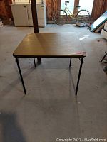 Folding square card table with metal legs and light wood laminate surface.
