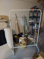 View of mop bucket, brooms, shovels, clothing rack in a basement or garage corner