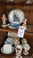 Shelf display with Goebel figurines, Royal Tara china bowls and plates, Lefton ceramic dish, and ceramic dry goods shakers with one broken