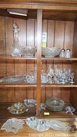 Full view of shelves displaying crystal and etched glass decanter, bowls, cordial glasses, pitchers, plates, and other serving pieces.