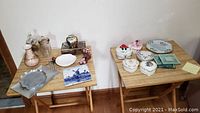 Photo shows two wooden folding tables with an assortment of decorative and collectible household items including music boxes, trinket dishes, coasters, decorative plates, and glass and metal collectibles.