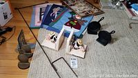 Photo shows Mary Engelbreit ceramic bookends, pineapple cast iron bookends, small cast iron skillet, metal stake, and fabric flags spread on floor and carpet.