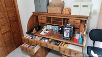 Overall view of wooden roll-top desk with various office supplies and organizers arranged on and in it.