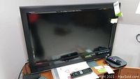 Vizio VO320E 32-inch LCD HDTV with remote and additional items on stand.