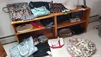 Photo showing multiple handbags and accessories arranged on two wooden shelves and floor, highlighting variety of Vera Bradley and other fabric bags.