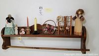 Full view of the Amish style wooden wall shelf quilt rack with folk art decor items arranged on it: angel dolls, small quilt rack with dried flowers, floral basket, and candles.