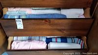 Several bath towels folded inside a drawer, showing assorted colors including white, blue, pastel pink and striped pattern.