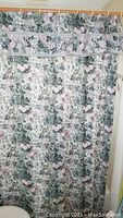 Floral fabric shower curtain with valance hanging on a rod, showing floral pattern in green and pink tones.