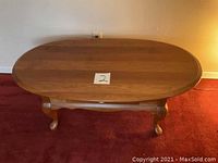 View of the coffee table from an angle showing the wood grain on the oval surface and one leg detail