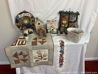 Group photo of all items including scarecrow dolls, birdhouses, quilted throw, fabric runner, and ceramic pot on white backdrop