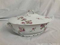 Side view of white china soup tureen with pink floral decoration, lid on, showing handle with gold accent and decorative edge.