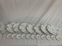 Wide view of 8 luncheon plates and 11 butter plates arranged in a row against white fabric background.