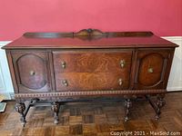 Front view showing the detailed wood grain on cabinet doors and drawers, brass hardware, and decorative carved molding around the edges and legs.