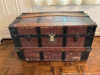 Closed antique steamer trunk showing weathered exterior with metal reinforcements and clasps.