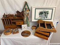 Full lot of assorted wooden decorative items on a white cloth, includes mail rack, boxes, butterfly holder, framed print and more