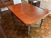 Angled view of solid wood dining table showing the rich brown finish, turned legs, and beveled octagonal tabletop edges.