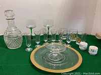 Full view of glassware including decanter, cordial glasses, custard cups, pedestal dish and plate arranged on green cloth