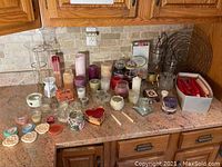 Overview of assorted candles, candle holders, wax melts, and taper candles arranged on a kitchen counter.