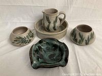 Five handcrafted pottery items arranged: three bowls, one pitcher with a base plate, and one dark glazed redware ashtray.