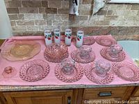 Photo of full glassware set on kitchen counter including yellow platter, pink bowl, candleholder, sundae cups, drinking glasses, and pink plates