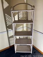 Front view of the tall rattan shelving unit with four shelves, showing arched top and lattice back panel.