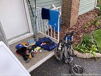 Golf bag caddy folded and resting beside a porch, golf clubs, accessories including caps and golf balls scattered on floor mat.