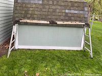 Full view of aluminum folding ladder scaffold standing on grass with platform panel attached between ladder sections.