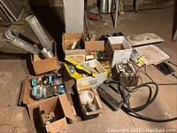 Photo showing boxes of assorted plumbing fittings, small tools, wiring and fasteners along with power steamer and cords on the floor.