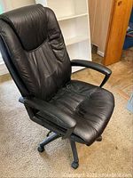 Black high back office chair with padded seat and back, black plastic armrests, and five-star wheeled base. Chair upholstery appears to be leather or similar material.