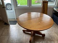 Round oak dining table with pedestal base seen from an angle showing tabletop and base; light finish with visible wood grain and natural color variations.