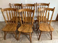Front view of six solid wood dining chairs with spindle backs and turned legs arranged on tile floor.