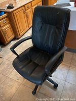 Front view of a single black high-back office chair with padded arms and caster wheels, placed in a kitchen setting.