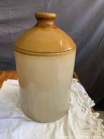 Front-facing view of the antique crock showing the light beige body and warm brown lid with glossy glaze.