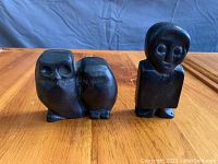 Front view of both carvings, showing the Boy and Girl Owl and The Apostle with their distinct shapes and carved faces.