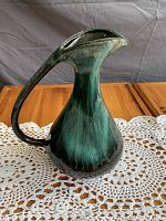 Side angle view showing the handle arching from the spout to midsection, glossy green gradient glaze on ceramic vase.