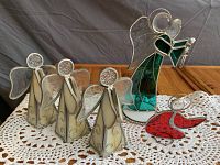 Five stained glass angel figurines displayed on a white lace cloth on a wooden table under natural light.