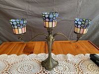 Full view of the iron candelabra with three stained glass candle holders on a wood surface with a crochet doily underneath.