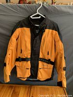 Front view of orange and black Joe Rocket safety coat showing protective padding on elbows and adjustable straps