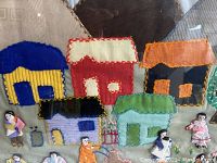 Close-up of colorful fabric houses with attached fabric figures in traditional clothing.