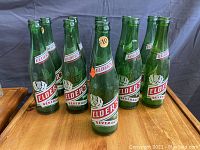 Front angle view of ten vintage green glass soda bottles with Elder's Beverage labels showing the overall condition and design of the bottles.