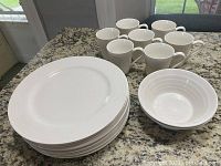Photo showing 7 white ceramic mugs, 8 dinner plates stacked, and 2 bowls on granite countertop.